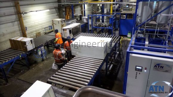 Refrigerator recycling machine in the back with roller conveyors that carry fridges. 